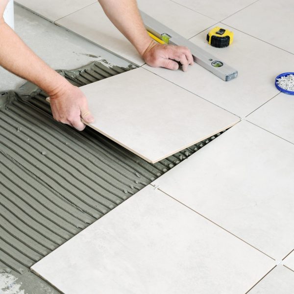 The hands of the worker are laying  the ceramic tile on the floor.